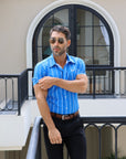 Man in a blue striped shirt standing in front of a house entrance.