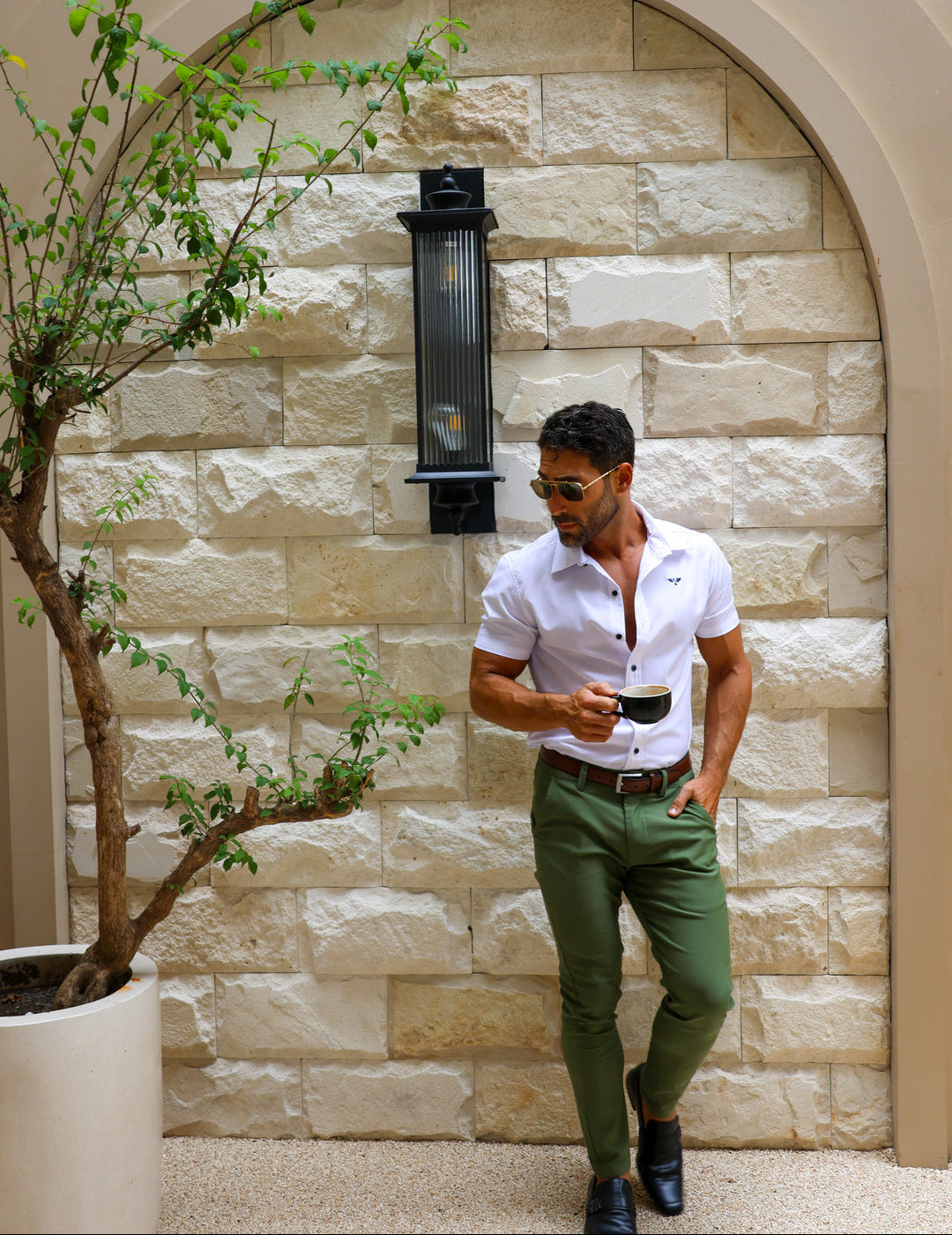 Man in a white shirt and olive Luxe Chino walking through a limestone courtyard