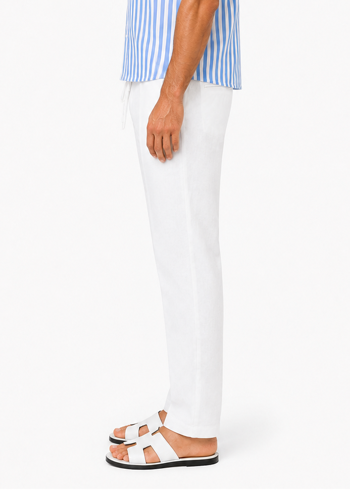 A man shown in profile wearing a light blue and white vertically striped short-sleeve button-up shirt, white trousers, and white slide sandals against a plain white studio background.